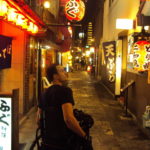 a man in a wheelchair, sat in a narrow pedestrian way - looking at a building sign