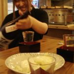 waitress fills the sake glass until it overflows into the masu (box)